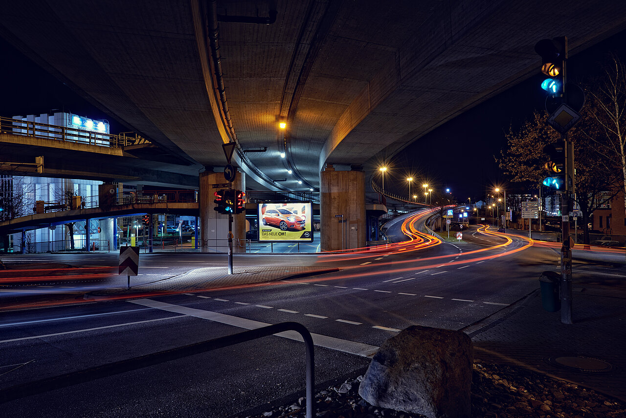 Beleuchtetes Großplakat unter einer Straßenbrücke mit Motiv von Opel, umgeben von vorbeiziehenden Autos und Lichtspuren – buchbar über Plakat-verkauft.de.