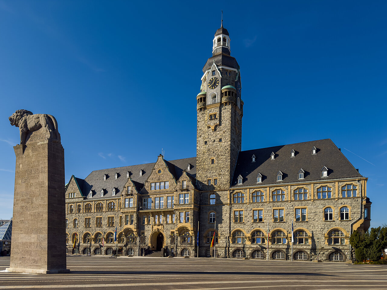 Das Bild zeigt den Remscheider Rathausplatz bei strahlend blauem Himmel. Davor steht die Statur des bergischen Löwens.