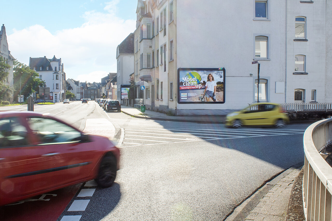 Großplakat an einer Hauswand montiert. Das Haus steht direkt an einer stark befahrenen Straßenkreuzung.