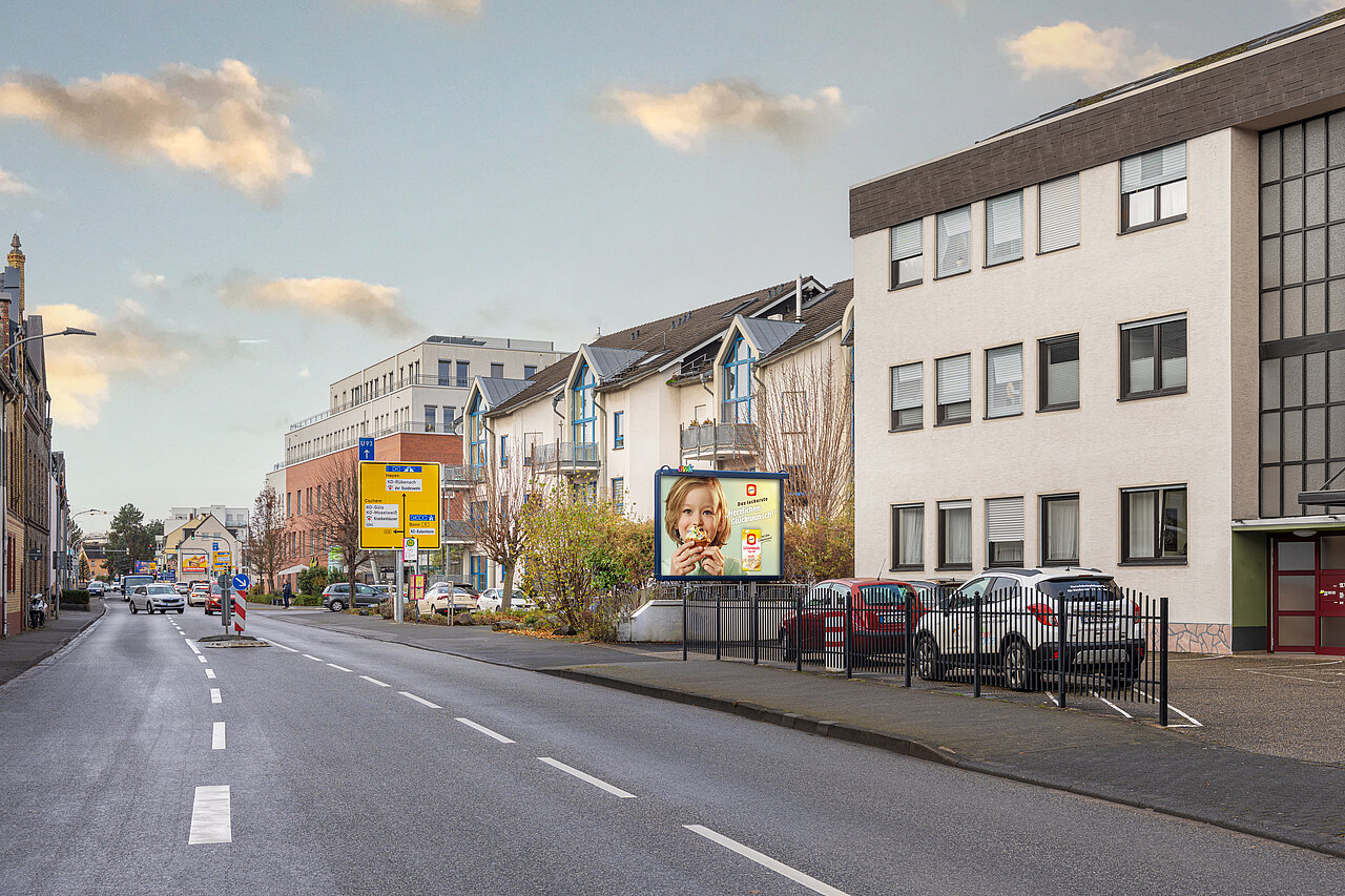 Eine Großfläche, montiert auf dem Grundstück eines Mehrfamilienhauses, welches sich an einer gut befahrenen Straße befindet.