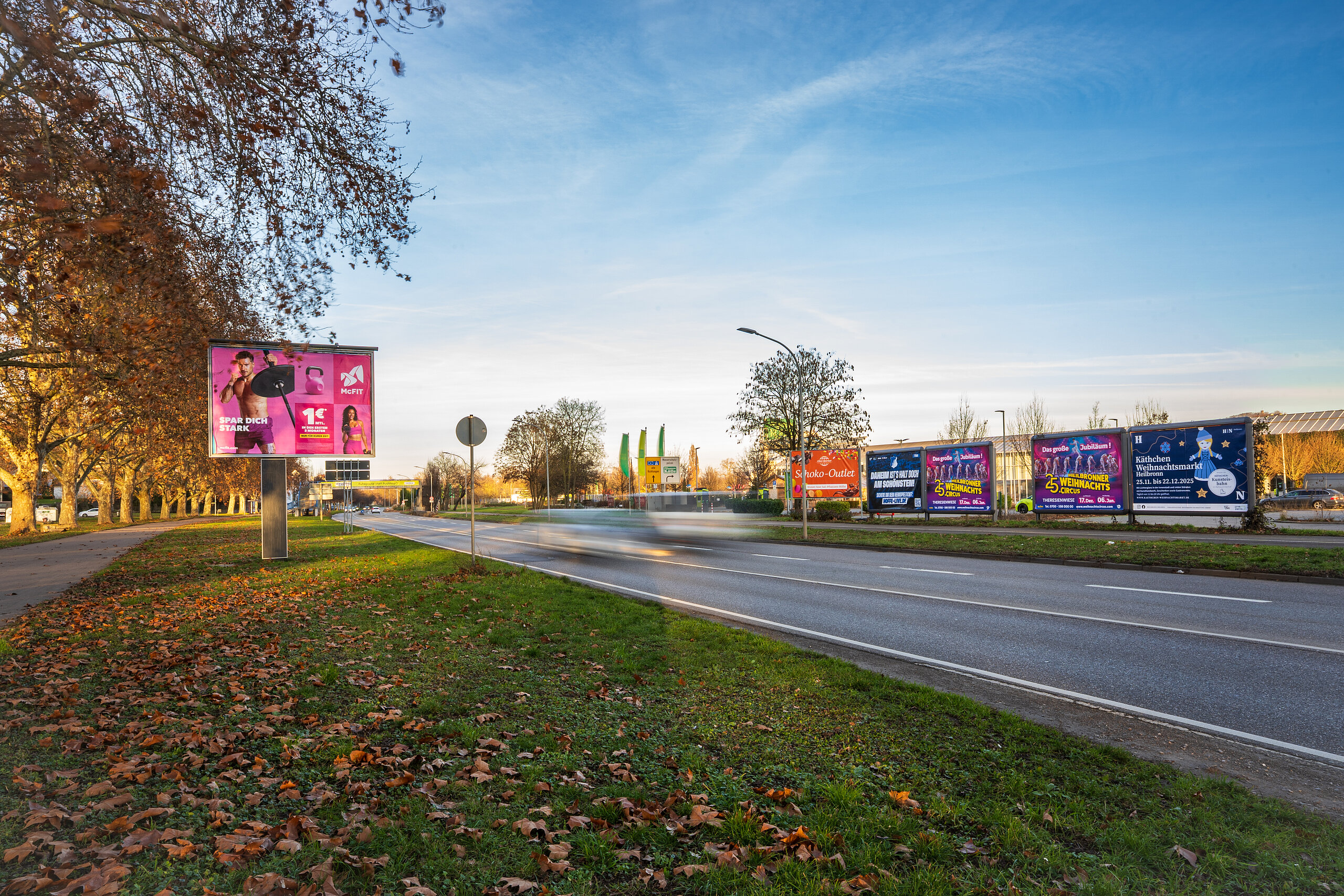 Mehrere Großflächen am Straßenrand beleuchtet bei Sonnenuntergang. 