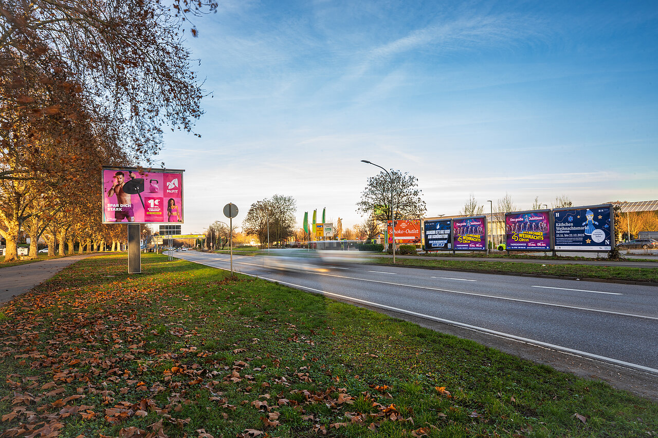 Mehrere Großflächen am Straßenrand beleuchtet bei Sonnenuntergang. 