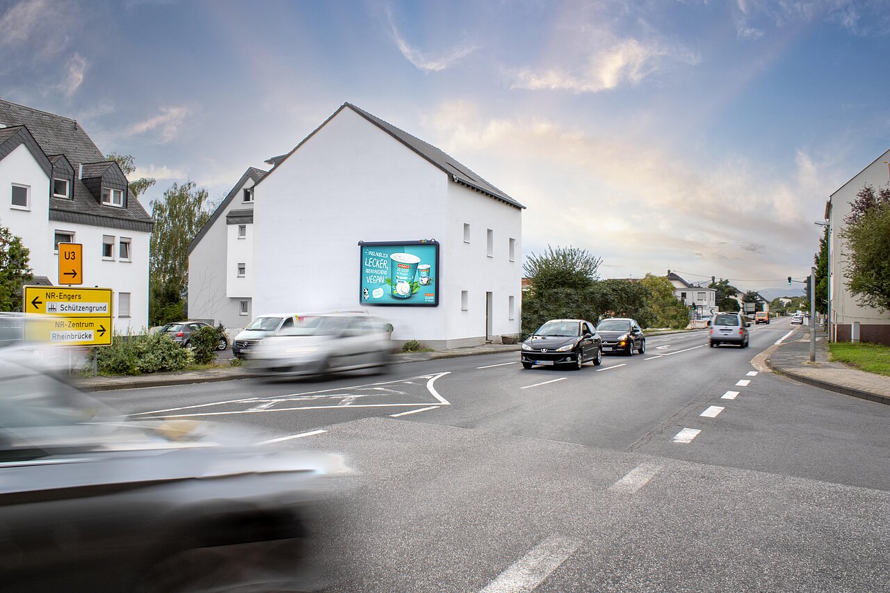 Großplakat an einer Hauswand montiert. Das Haus steht an einer stark befahrenen Straßenkreuzung..