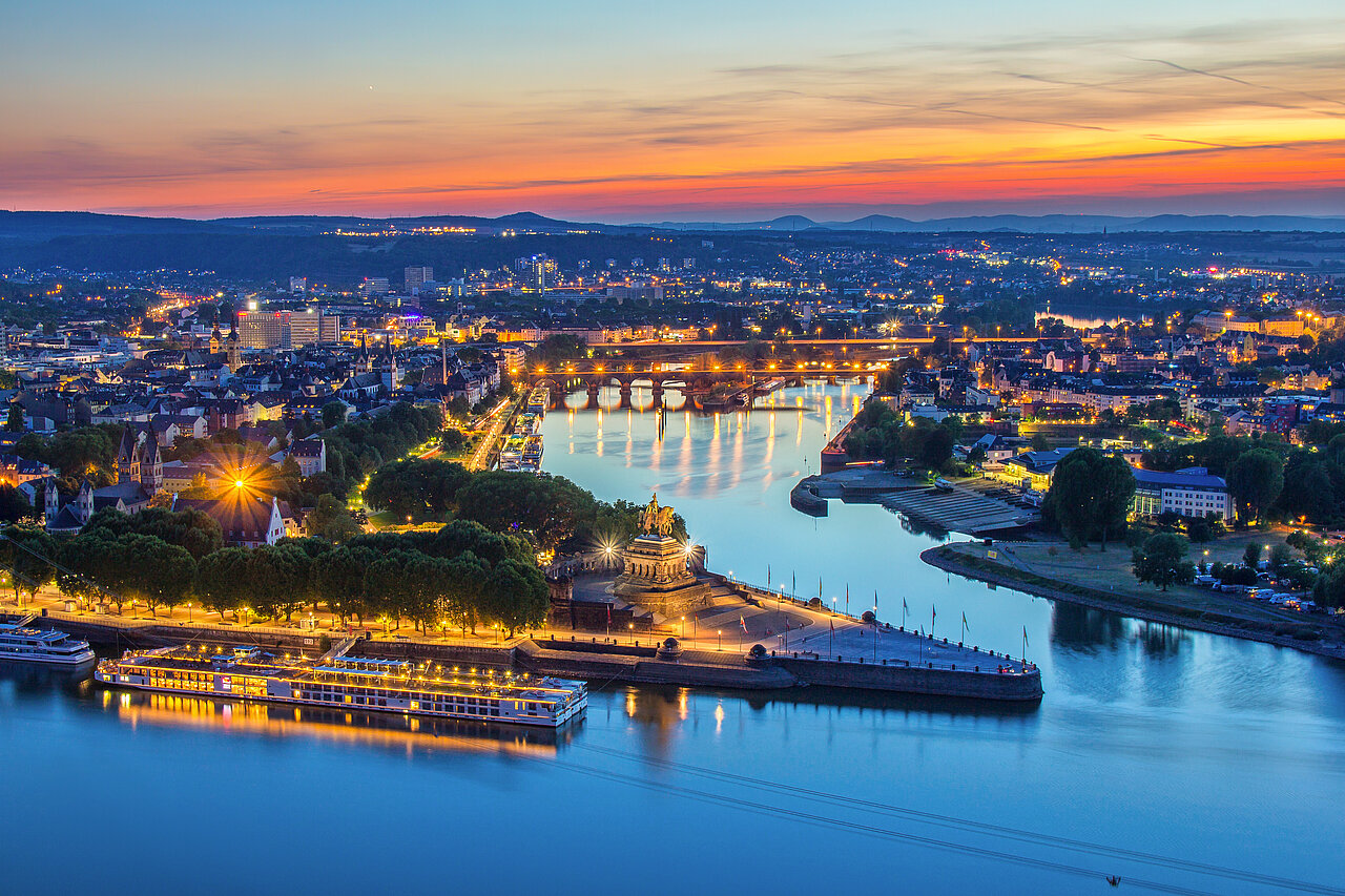 Blick auf das Deutsche Eck in Koblenz bei Sonnenuntergang: Zusammenfluss von Rhein und Mosel, historische Kaiser-Statue und Flusspromenade.