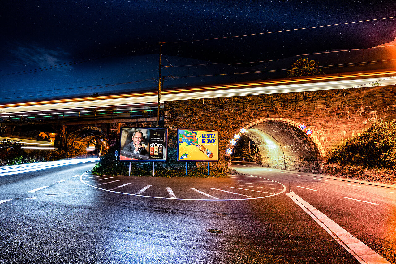Zwei Großplakate an einer Straßenunterführung bei Nacht.