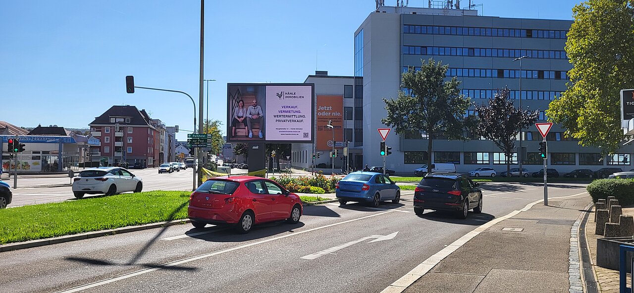 Digitale Großfläche: Motiv von der Firma "Hänle Immobilien" mit der Aufschrift "Verkauf, Vermietung, Wertermittlung, Privatverkauf", daneben ein Foto von 2 Mitarbeitern sitzend auf einer Treppe. 