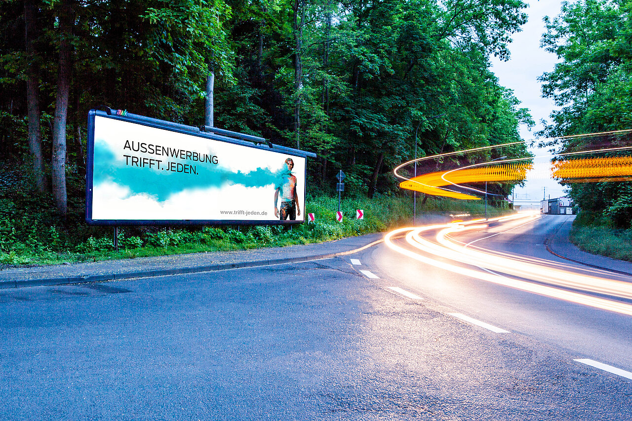 Ein beleuchteter Megastar am Straßenrand zeigt eine klare Werbebotschaft: „Außenwerbung trifft. Jeden.“