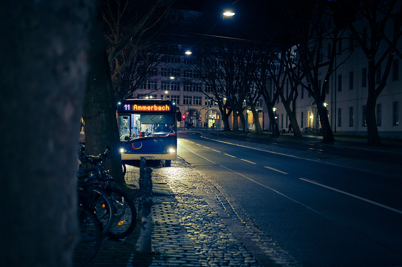 Bushaltestelle in Jena bei Nacht, beleuchtet von Straßenlaternen, an der ein Bus hält.