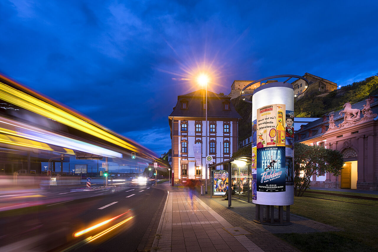 Abendstimmung in der Stadt – eine beleuchtete Werbesäule zieht alle Blicke auf sich. Direkt an der Bushaltestelle platziert, sorgt sie für maximale Sichtbarkeit im urbanen Raum.