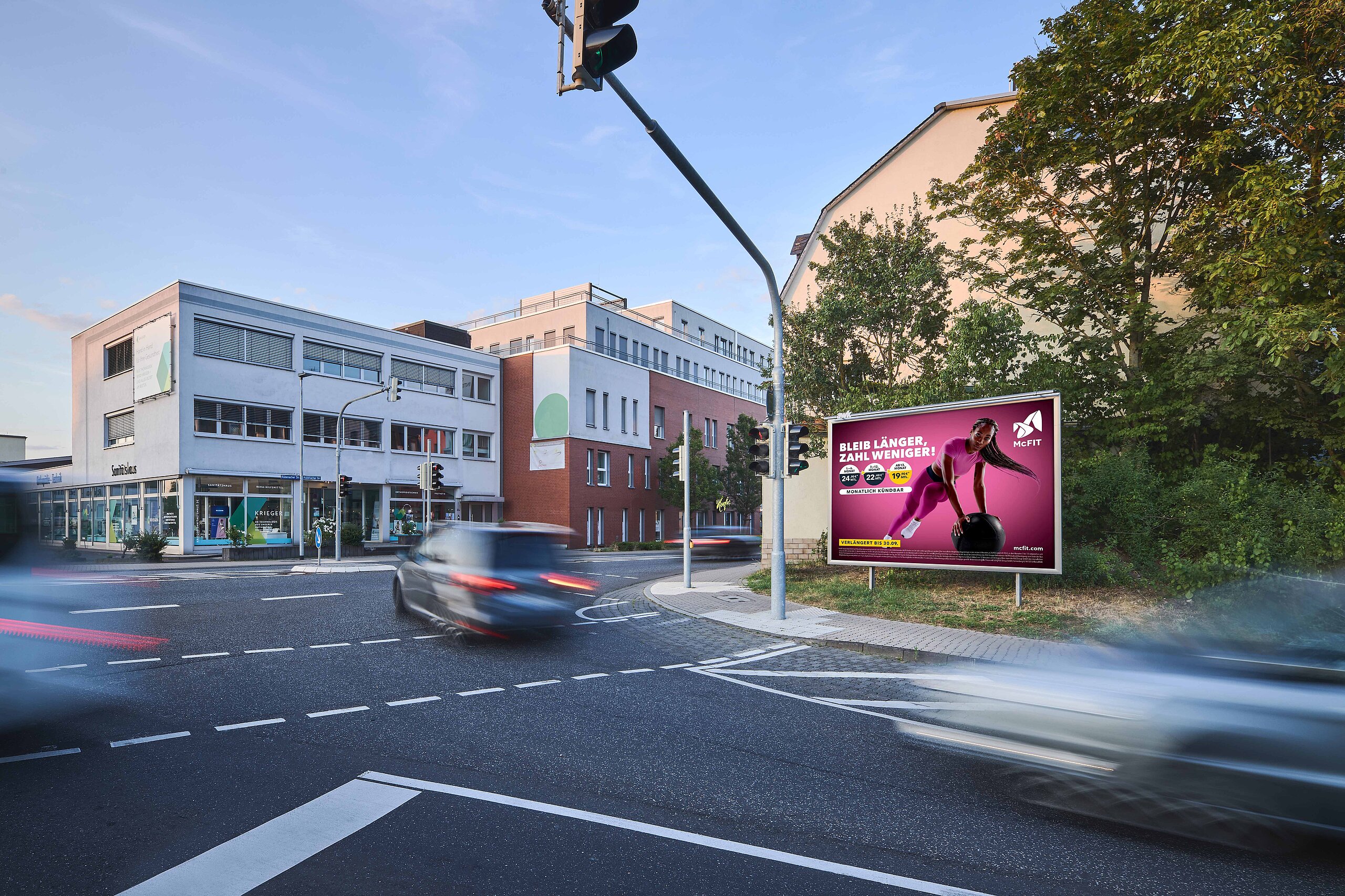 Werbeplakat an einer gut sichtbaren Straßenecke, das eine sportliche Frau beim Training zeigt. Durch die Platzierung an einem belebten Knotenpunkt zieht das Plakat sowohl Autofahrer als auch Fußgänger an und sorgt für hohe Reichweite.