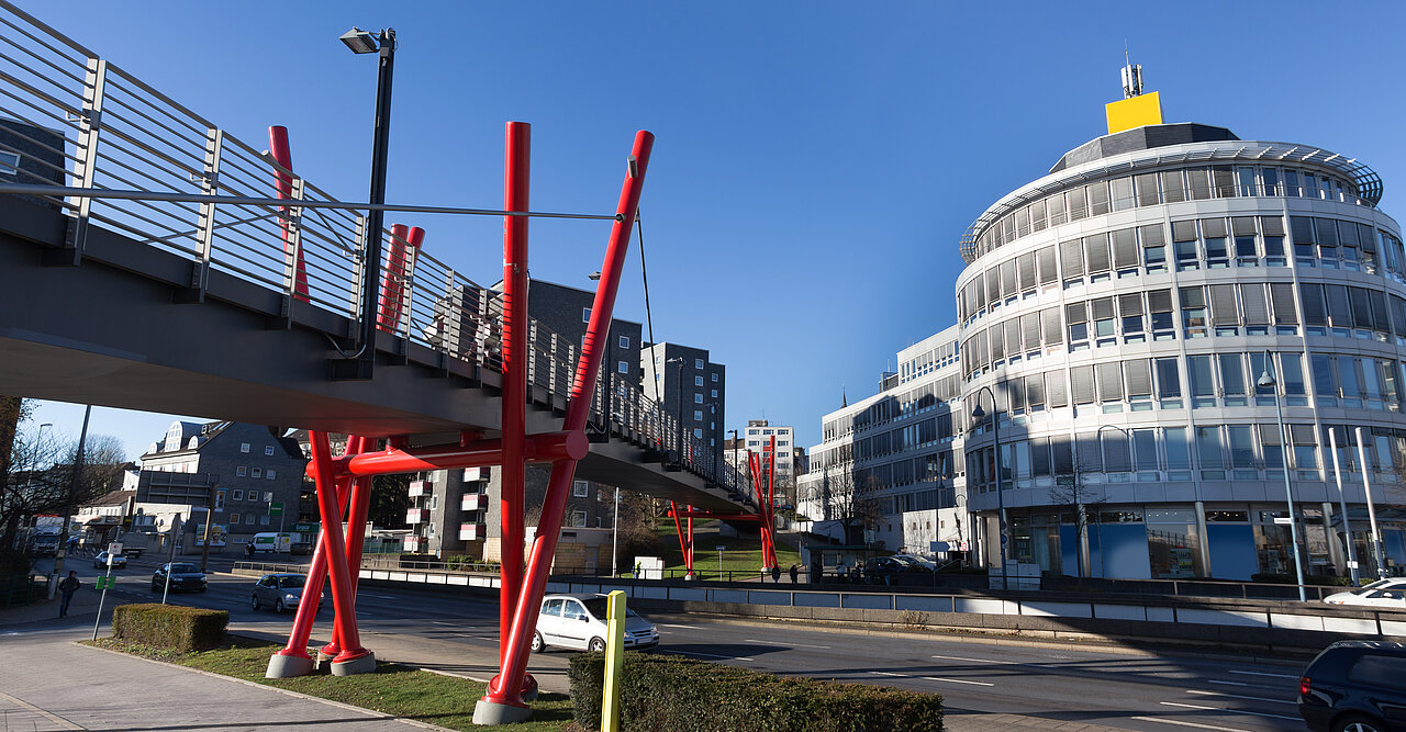 Das Bild zeigt die Fußgängerbrücke in Remscheid über den neu gestalteten Bahnanlagen von Remscheid Hauptbahnhof, Wartehalle links auf dem Bahnsteig, Geschäftsgebäude hinter den Gleisanlagen