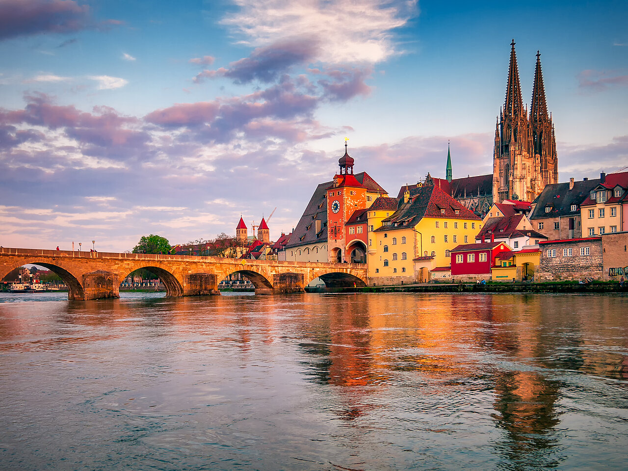 Panoramablick auf die Altstadt von Regensburg vom Ufer aus, mit historischen Gebäuden und steinerner Brücke entlang des Flusses.