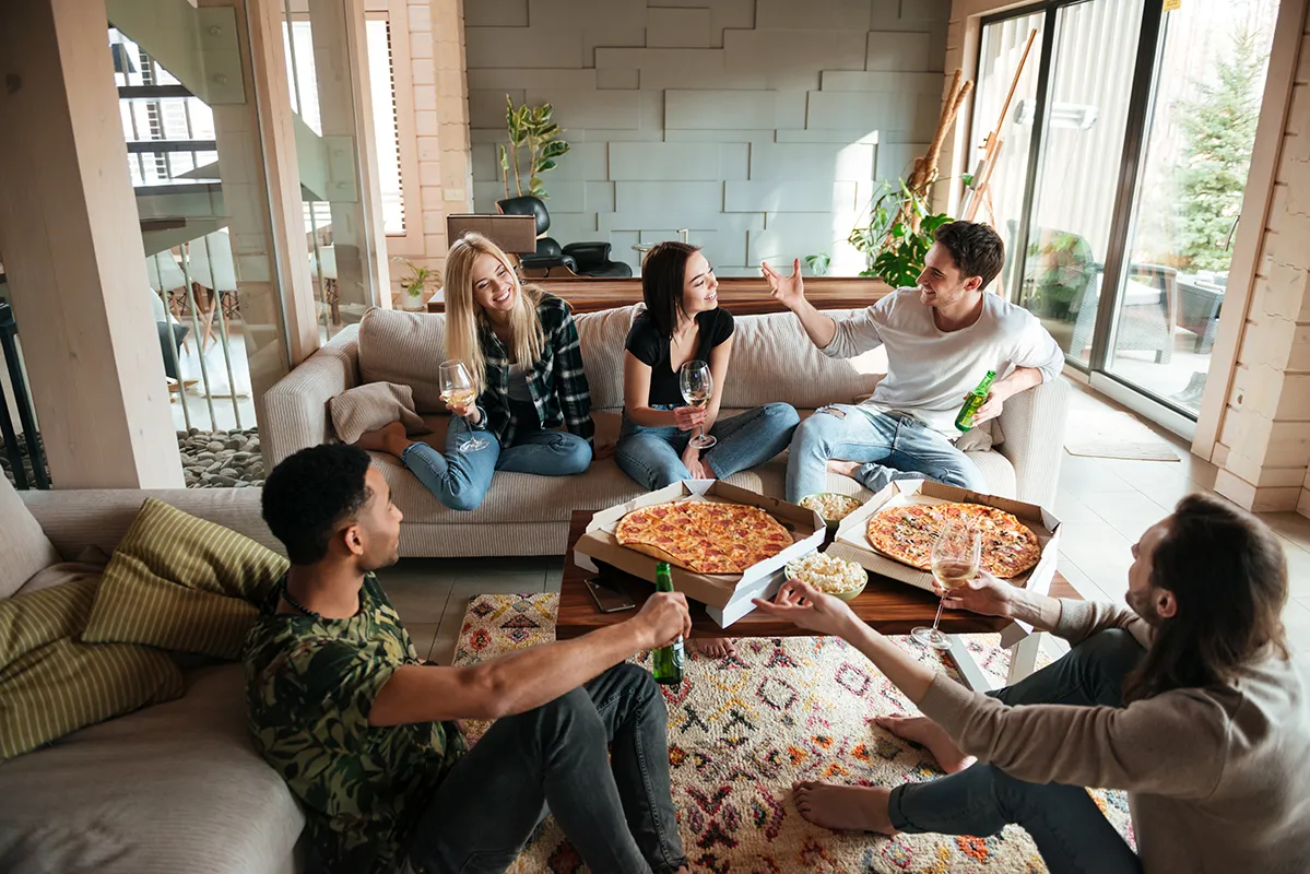 Freunde essen Pizza im Wohnzimmer Gruppe junger Menschen isst Pizza und trinkt gemeinsam im Wohnzimmer.