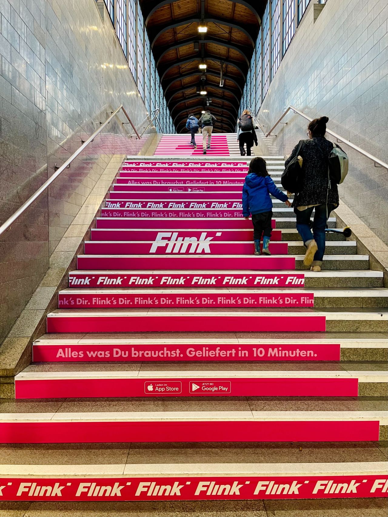 Mit pinken Floorgraphics beklebte Bahnhofstreppe mit Flink-Werbung, während Passanten die Stufen hinaufgehen.