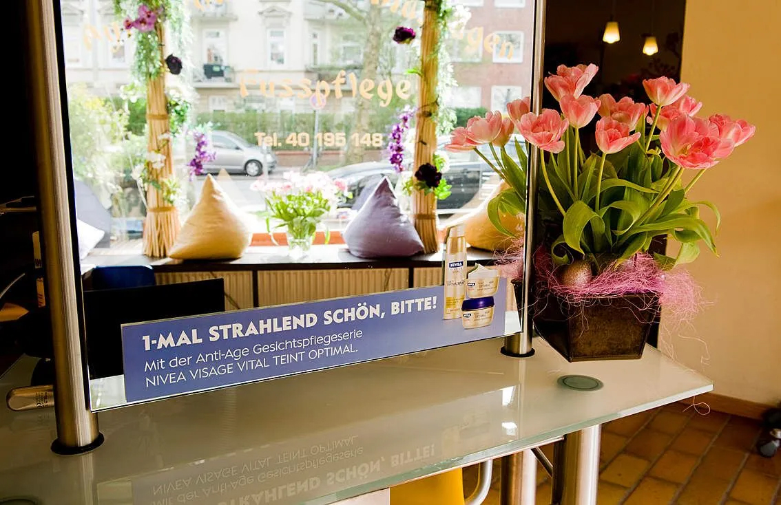 Werbeplakat der Marke Nivea, das an einem Spiegel in einem Beautysalon angebracht ist – Beispiel für effektive Spiegelwerbung im Pflege- und Stylingbereich.