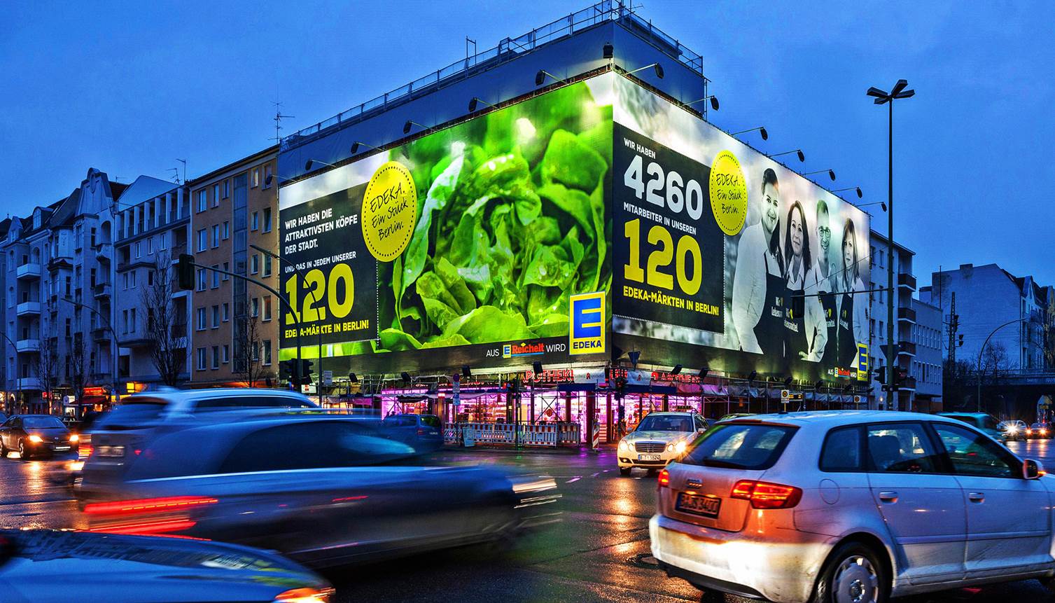 Riesenposter auf einem Gebäude in der Stadtmitte mit einer Werbung für EDEKA. Große, leuchtende Plakate in XXL-Format an einer stark befahrenen Straße mit Abendbeleuchtung.